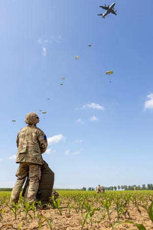 a soldier looks up at parachutists falling from an airplane in the sky