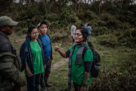 A woman holds up a plant for three people around her to see in a green landscape