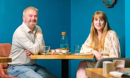 A man and a woman sitting at a restaurant table in front of a blue wall