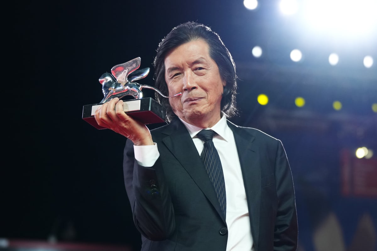 A man in a suit and tie grins as he holds up an award.