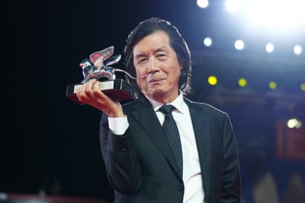 A man in a suit and tie grins as he holds up an award.