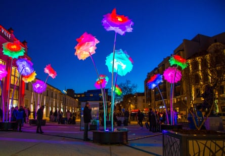 Giant colourful glowing flower sculptures tower over a plaza at dusk