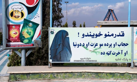 An amusement park ride can just be seen above a sign showing a veiled woman facing writing in Pashto.