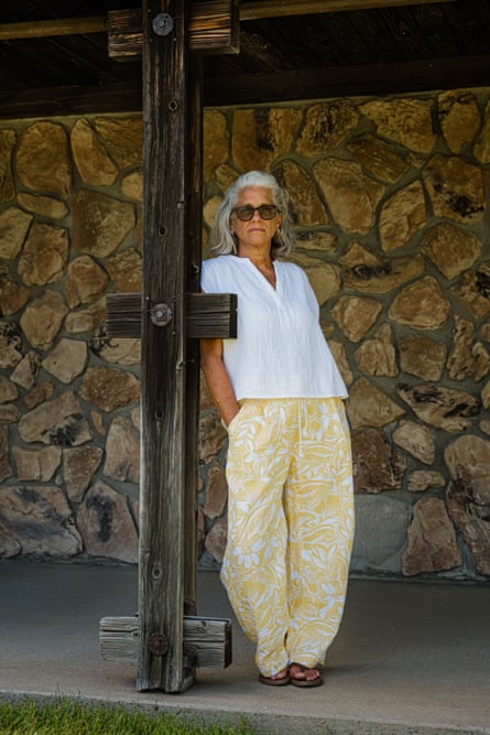 woman in white shirt and printed yellow pants leans against post outside building