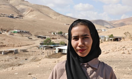 Alia Mlehat, from al-Mu’arrajat – young woman wearing black headscarf and red lipstick, standing against stark landscape