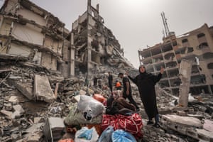 A woman gestures next to bags of belongings amid the rubble of a building