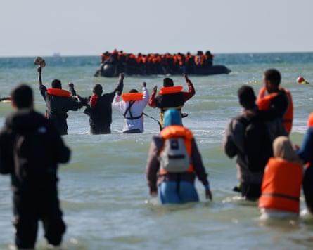 People wading out in water off the French coast, with a crowded dinghy in the distance