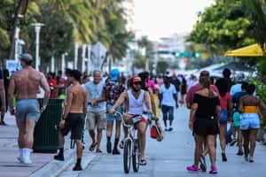 A man rides a bicycle as people walk on Ocean Drive in Miami Beach, Florida on June 26, 2020. Florida has registered more than 15,000 new cases of coronavirus in a day, easily breaking a record for a US state previously held by California, according to official numbers published on July 12, 2020.