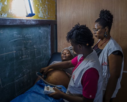 A pregnant Haitian woman lying on a medical trolley while examined by two members of a medical team