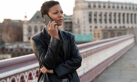 A still from Industry of a woman wearing a black leather jacket standing outside as she talks on the phone
