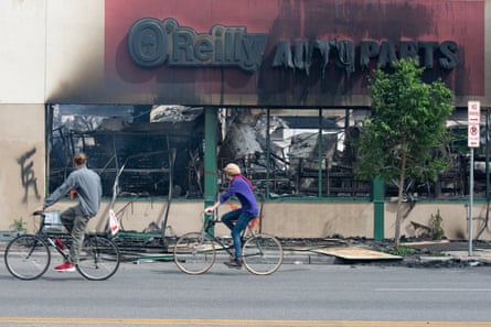 Cyclists ride past the burned out O’Reilly Auto Parts store in Minneapolis.