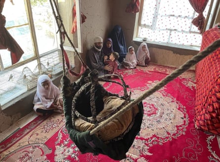 A woman in a burqa sits in a corner of a barely furnished room with her five young children and husband