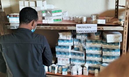A man wearing a face mask with his back to the camera at a shelf stocked with boxes of vaccines