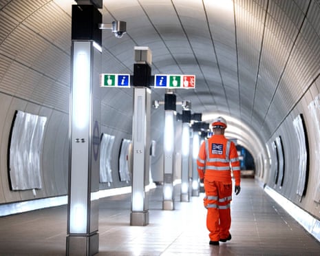 A worker in an orange hi-vis suit walks through the Elizabeth Line tunnel walkway