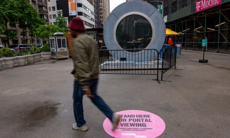 a man walks past a large circular installation on a city street surrounded by buildings