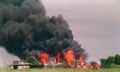 The compound in Waco, Texas, with billowing black clouds and two-storey flames in a field next to trees