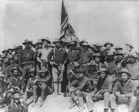 A black and white photograph of US troops posing around the US flag