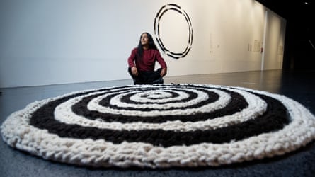 Antonio Paucar sits on the gallery floor behind his large woven alpaca wool sculpture, a black and white spiral.