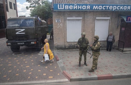 A woman walking past a couple of armed Russian servicemen standing guard outside a centre for the preparation of documents for the registration of Russian citizenship and passport application, in Melitopol