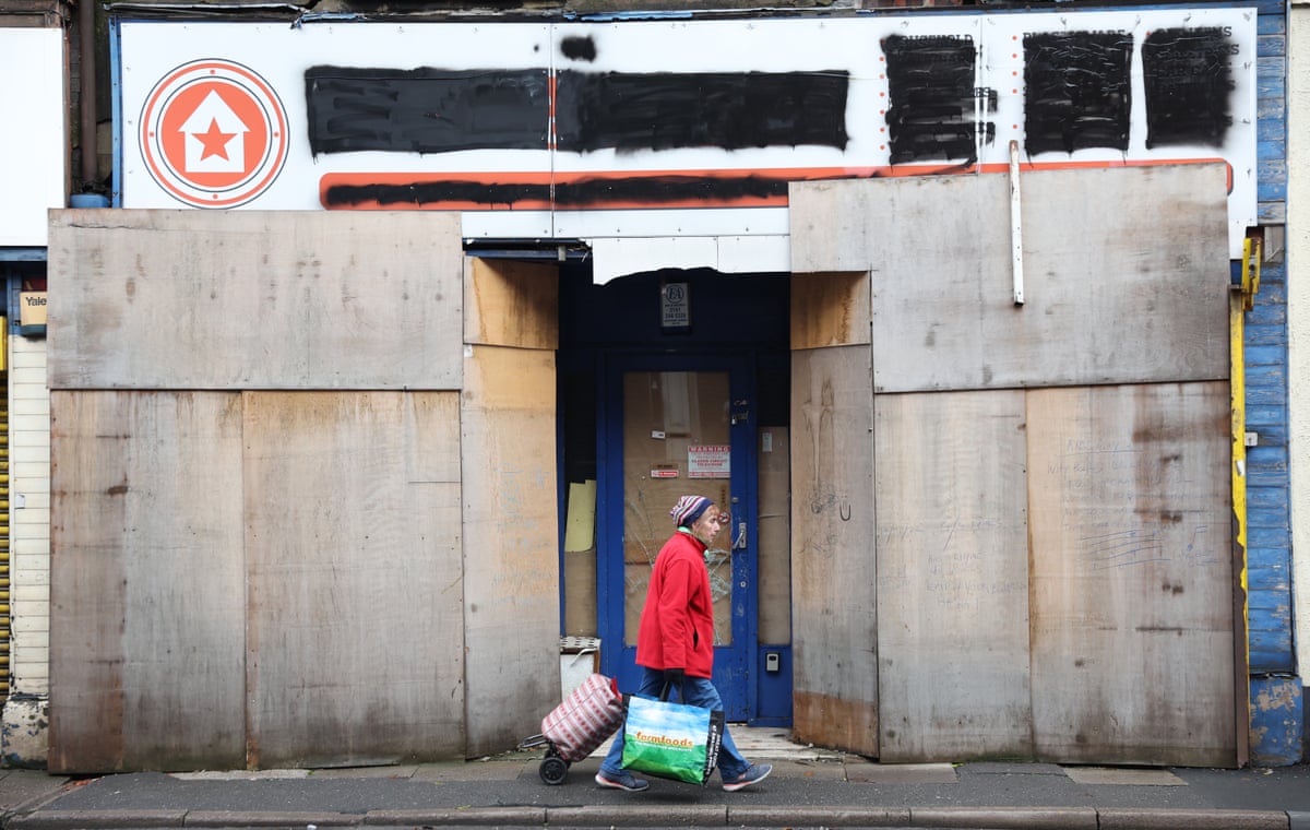 A lady walks past a boarded up shop in Longton on in Stoke-on-Trent, England wiht a shopping trolly and bag for life.