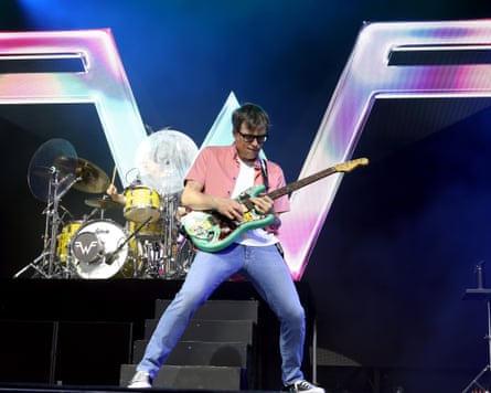 He noodles intensely on his guitar while playing on stage in front of a drum kit