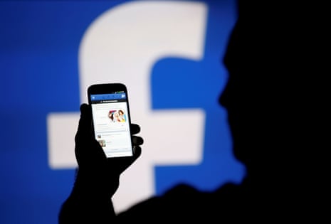 A man silhouetted against a video screen with a Facebook logo