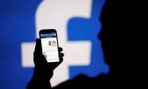 Silhouetted man holds phone in front of Facebook logo