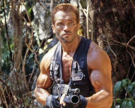 Arnold Schwarzenegger wearing a vest and camouflage makeup and holding a large gun