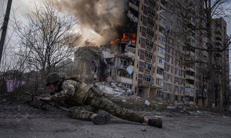 A Ukrainian police officer takes cover near a burning building that was hit in a Russian airstrike in Avdiivka, Ukraine