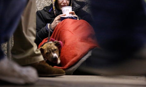 A homeless woman sits as pedestrians pass by