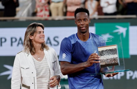Tournament director Amelie Mauresmo looks on as Gaël Monfils poses with an award at his farewell ceremony.