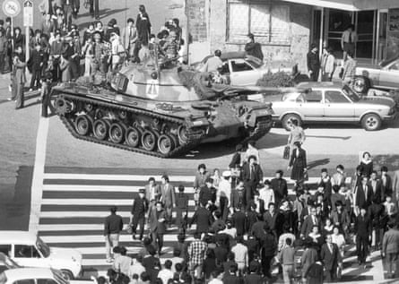 A tank driving though a city intersection amid crowds of people