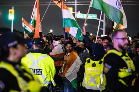 People gather and wave the Indian flag as police assemble in the foreground.