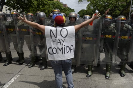 A woman with a sign reading “There is no food” protests against new emergency powers decreed by President Maduro in front of a line of police officers.