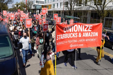 People march in a street with pro-union signs supporting Starbucks and Amazon workers.