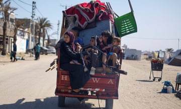 A Palestinian family on a truck with all their belongings seen from the back on a road with a shopping trolley and tents