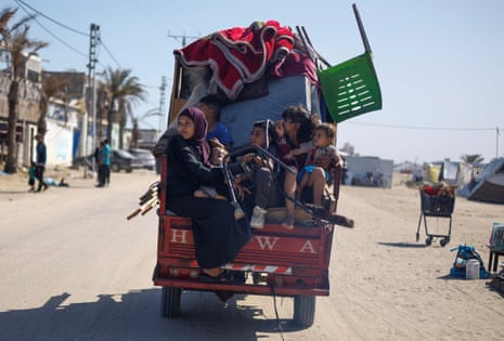 A Palestinian family on a truck with all their belongings seen from the back on a road with a shopping trolley and tents