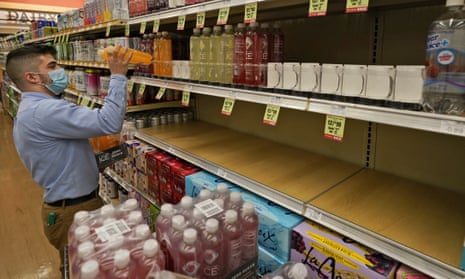 A man wearing a blue medical mask stocks empty shelves with drinks at a grocery store.