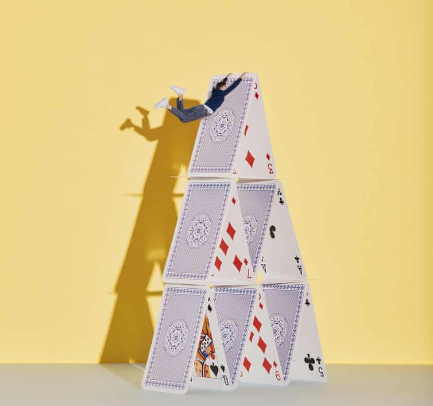 A tiny man clinging to the top of a card house