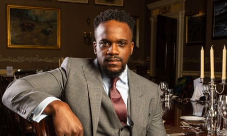 Samuel Kasumu in suit and tie in RAC club Pall Mall surrounded by paintings and candlesticks