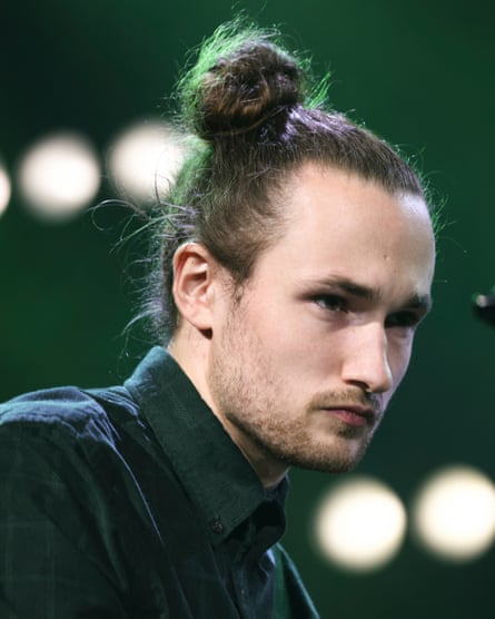 Fergus McCreadie en chemise boutonnée et cravate, avec une légère barbe et ses longs cheveux en chignon, l'air sérieux
