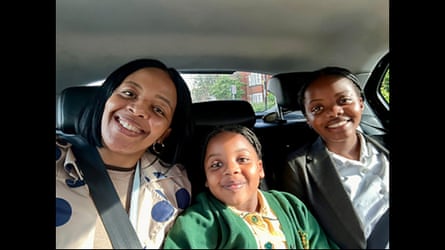 A woman in the back seat of a car with her two daughters; all three are smiling happily.