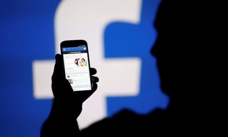 A man is silhouetted against a video screen with an Facebook logo