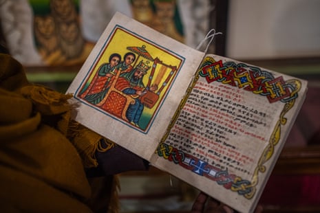 An open manuscript made of parchment with an ornate page of script on the right opposite a colourful illustrated page depicting a man wearing a crown seated on a throne with two people standing behind, one holding a sword.