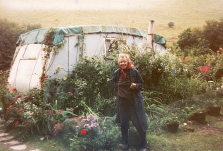 Bourne stood next to a caravan that is covered with flowers and other plants growing beside it and over it