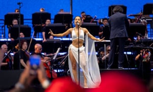 Becky G is singing with classical musicians sitting behind her