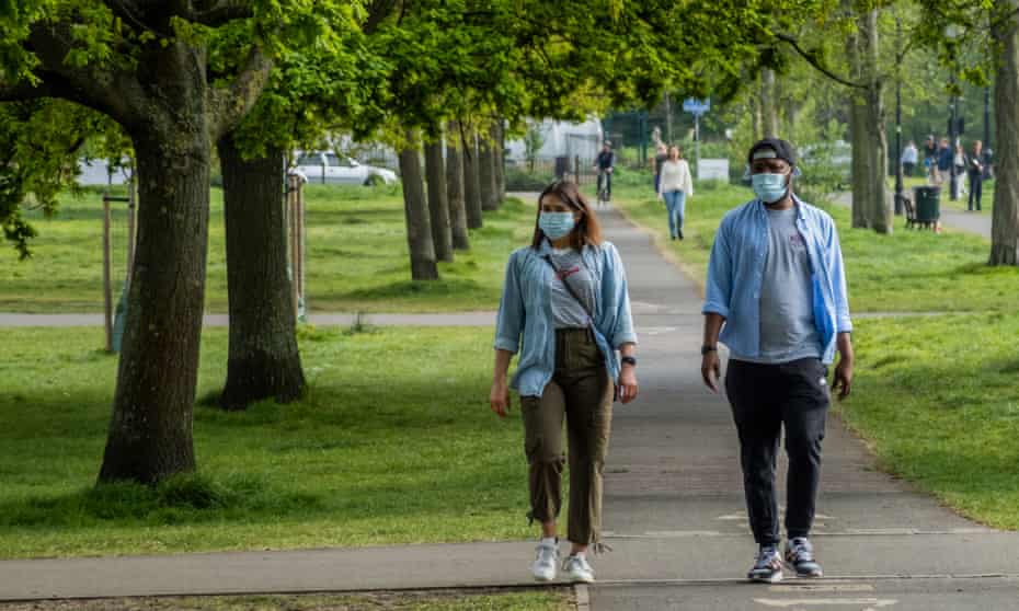 A couple walking in a park in London, both wearing face masks