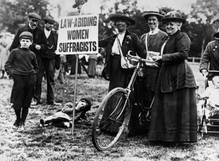 A black and white shot which shows suffragists standing alongside a bicycle and a placard which states “Law abiding women suffragists”.