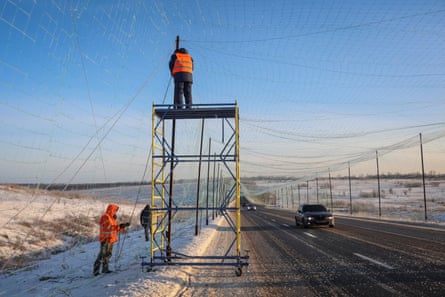 Workers installing anti-drone nets over a road in icy conditions near Kharkiv