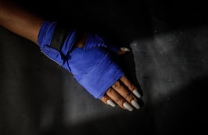 Esther's lower arm, showing boxer's handwrap (blue) with long, manicured fingernails, painted blue